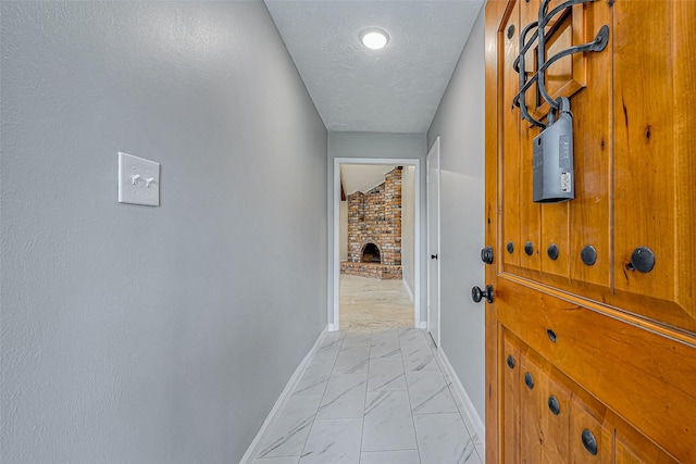 entryway with marble finish floor, a brick fireplace, a textured ceiling, and baseboards