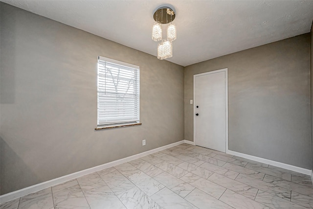 unfurnished room with an inviting chandelier, baseboards, and marble finish floor