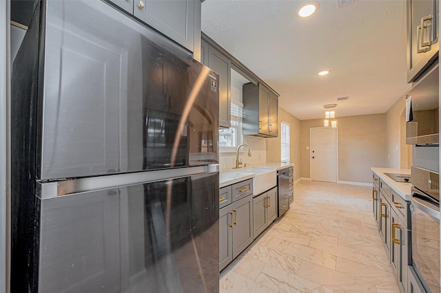 kitchen with a sink, marble finish floor, appliances with stainless steel finishes, and light countertops