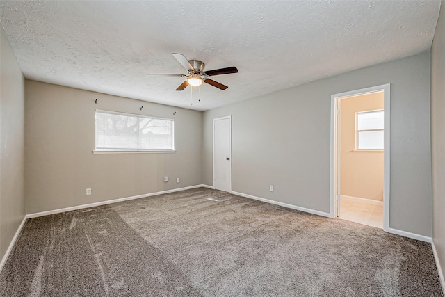 carpeted empty room with baseboards, a textured ceiling, and a ceiling fan