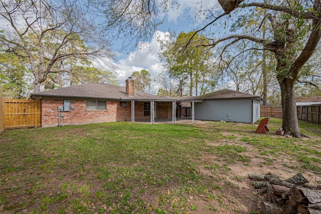 back of house featuring brick siding, a chimney, a yard, a fenced backyard, and a patio