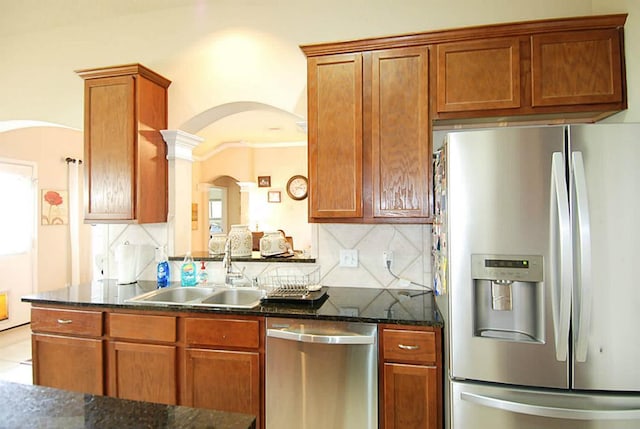 kitchen with a sink, dark stone countertops, arched walkways, appliances with stainless steel finishes, and decorative backsplash