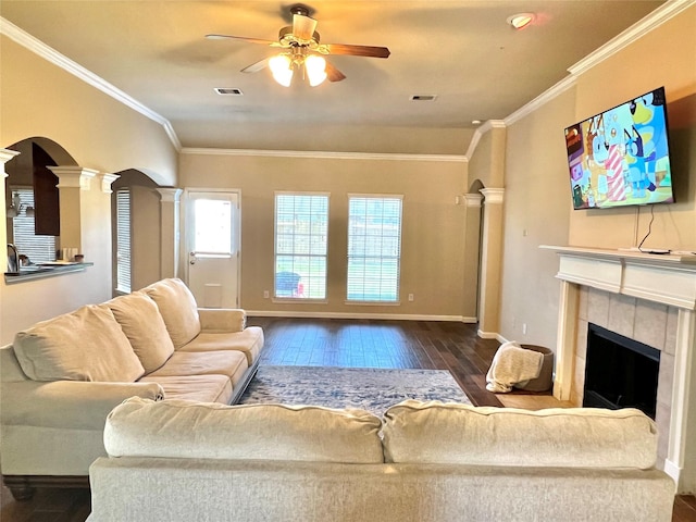 living room with wood finished floors, visible vents, ornate columns, a fireplace, and crown molding