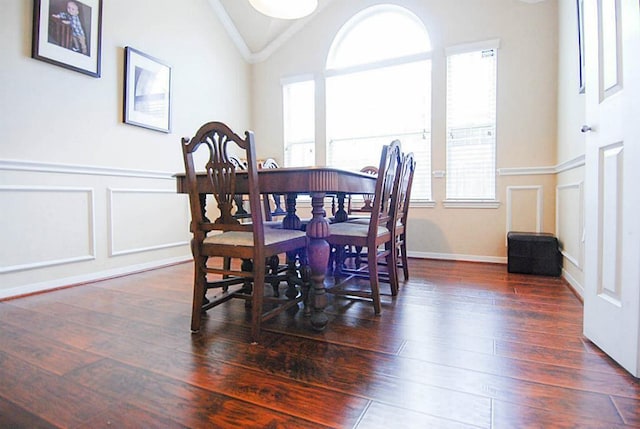 dining space with a decorative wall, wainscoting, dark wood-style flooring, and vaulted ceiling