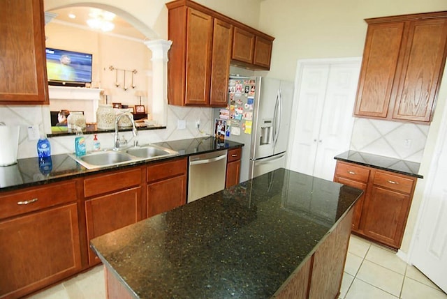 kitchen featuring decorative backsplash, appliances with stainless steel finishes, arched walkways, light tile patterned flooring, and a sink