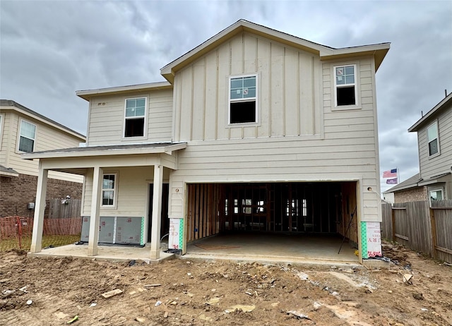 back of house with board and batten siding, an attached garage, and fence