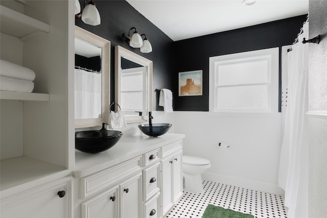 bathroom with a sink, baseboards, toilet, and double vanity