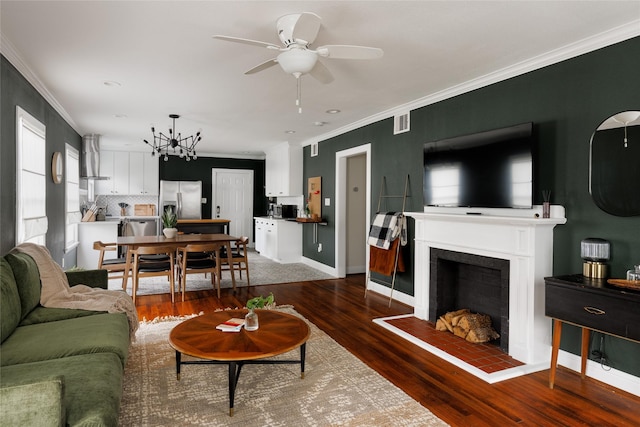 living room featuring a fireplace with raised hearth, visible vents, dark wood-style flooring, and ornamental molding