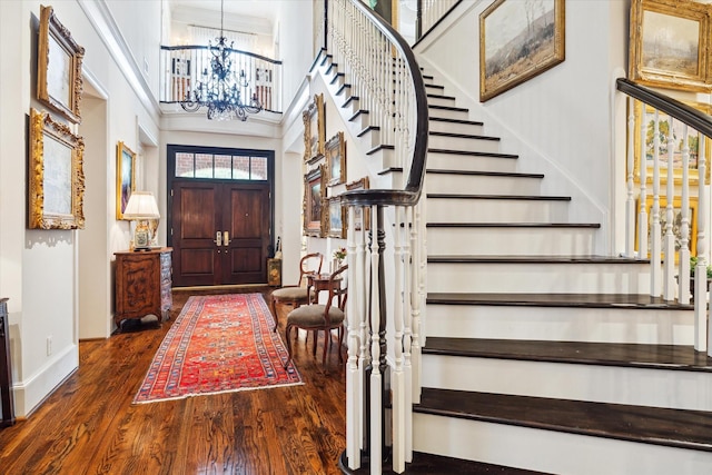 entryway with wood finished floors, baseboards, a high ceiling, stairs, and a notable chandelier