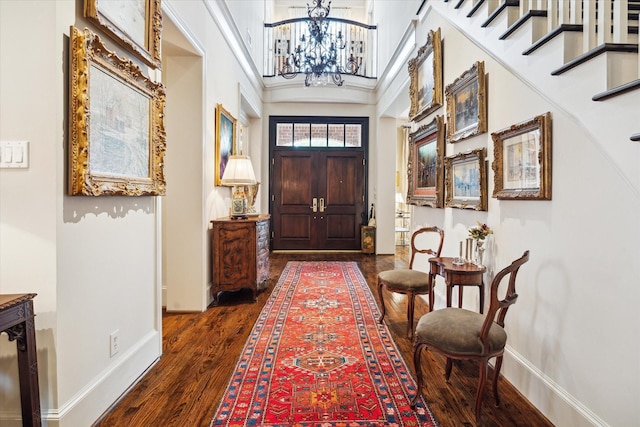 foyer with dark wood-style floors, a high ceiling, baseboards, a chandelier, and stairs