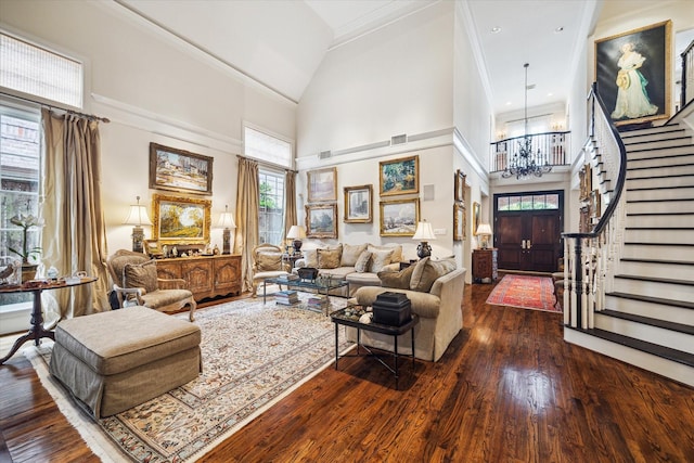 living room featuring stairway, ornamental molding, dark wood-type flooring, a towering ceiling, and a notable chandelier