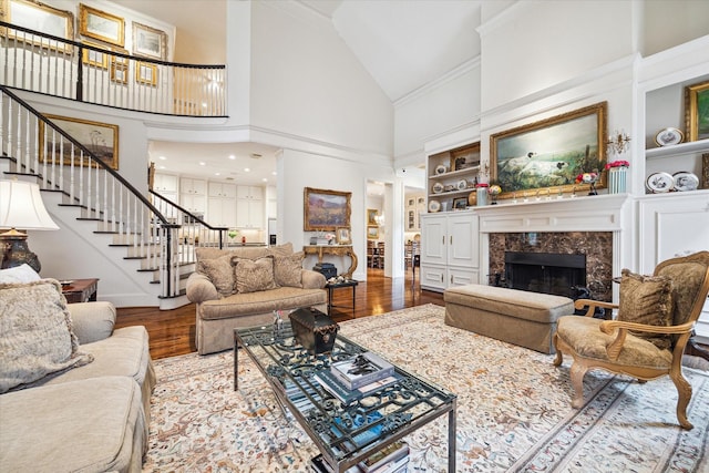 living room with high vaulted ceiling, built in features, wood finished floors, a premium fireplace, and stairs