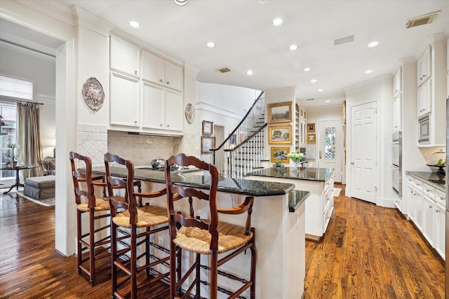 kitchen featuring dark wood-style floors, visible vents, a breakfast bar, decorative backsplash, and crown molding