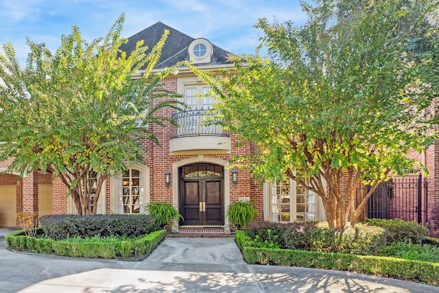 entrance to property with brick siding, a shingled roof, a balcony, and fence