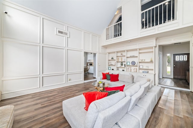 living room featuring a decorative wall, high vaulted ceiling, visible vents, and wood finished floors