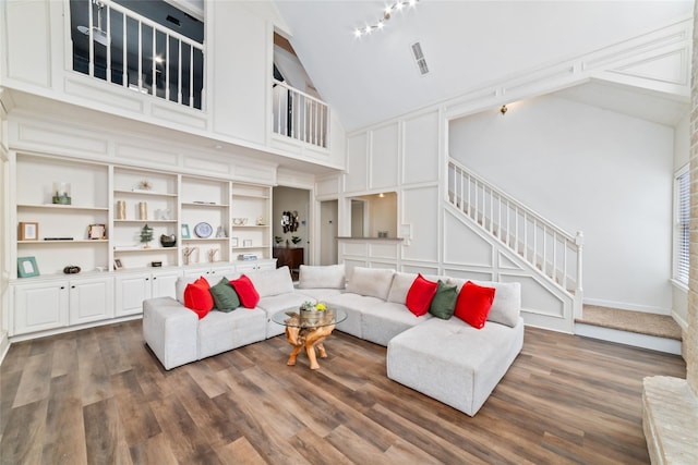 living room with high vaulted ceiling, wood finished floors, a decorative wall, baseboards, and stairs