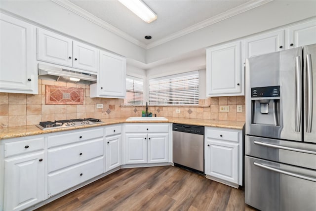 kitchen with a sink, under cabinet range hood, appliances with stainless steel finishes, white cabinetry, and crown molding