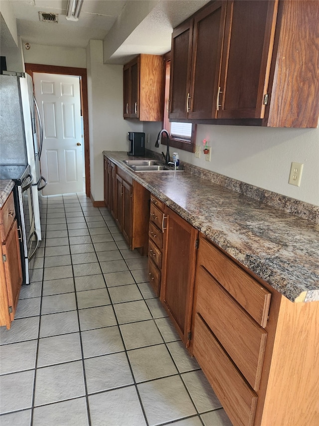 kitchen featuring dark countertops, visible vents, stainless steel range with electric stovetop, light tile patterned flooring, and a sink