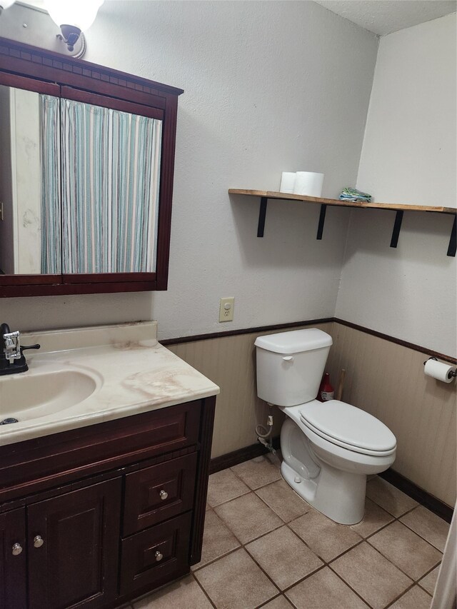 bathroom featuring vanity, wooden walls, a wainscoted wall, tile patterned flooring, and toilet