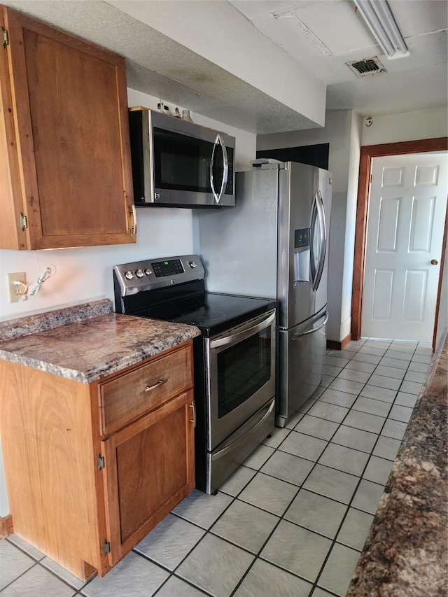 kitchen featuring light tile patterned floors, brown cabinetry, visible vents, stainless steel appliances, and dark countertops