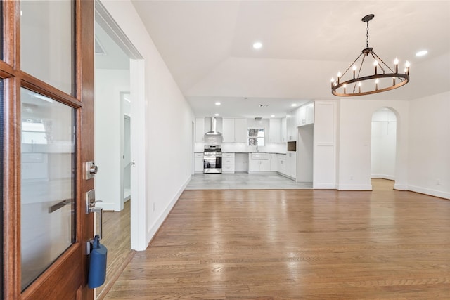 unfurnished living room featuring baseboards, recessed lighting, arched walkways, light wood-type flooring, and a chandelier