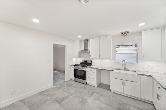 kitchen featuring a sink, stainless steel gas range oven, white cabinetry, wall chimney exhaust hood, and tasteful backsplash