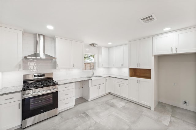 kitchen featuring visible vents, wall chimney range hood, light stone countertops, gas stove, and a sink