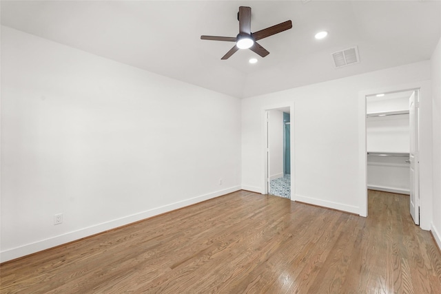 unfurnished bedroom featuring a walk in closet, wood finished floors, visible vents, and baseboards