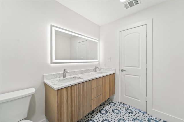 bathroom featuring a sink, visible vents, toilet, and double vanity