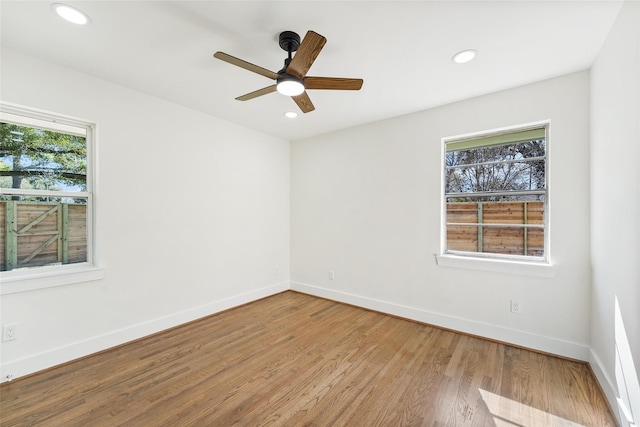 spare room with recessed lighting, plenty of natural light, wood finished floors, and baseboards