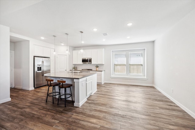 kitchen with a sink, dark wood-type flooring, appliances with stainless steel finishes, and an island with sink