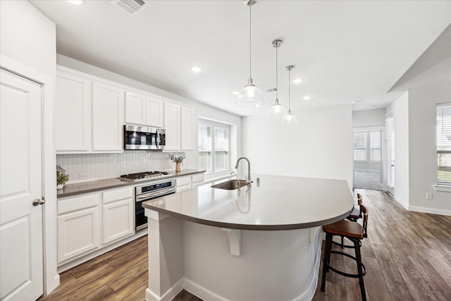 kitchen featuring backsplash, an island with sink, dark wood-style floors, stainless steel appliances, and a sink