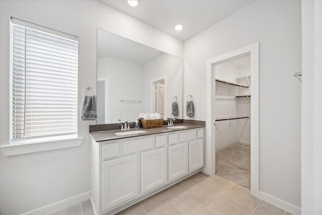 bathroom featuring double vanity, a walk in closet, baseboards, and a sink