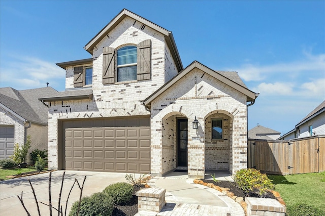 french country inspired facade with brick siding, an attached garage, driveway, and a gate