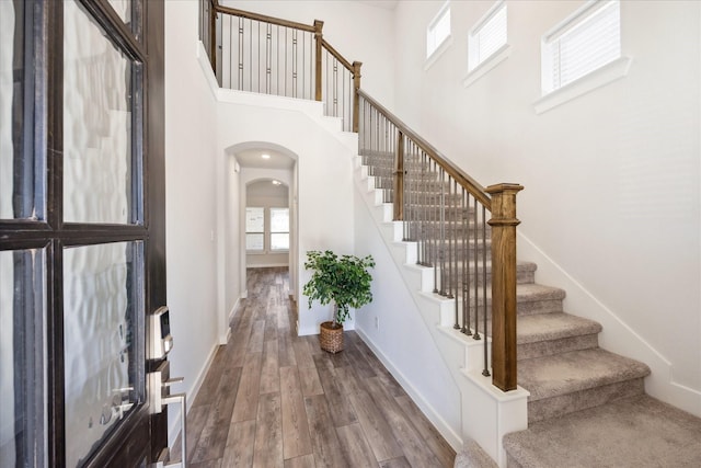 entrance foyer featuring wood finished floors, stairway, arched walkways, baseboards, and a towering ceiling