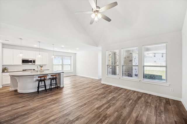 unfurnished living room with baseboards, high vaulted ceiling, wood finished floors, and a ceiling fan