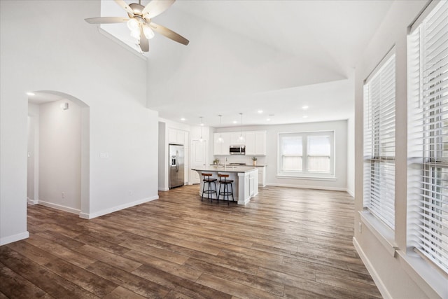 unfurnished living room featuring baseboards, a high ceiling, recessed lighting, arched walkways, and dark wood-style flooring