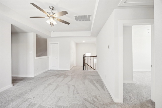 carpeted spare room featuring a raised ceiling, baseboards, visible vents, and ceiling fan