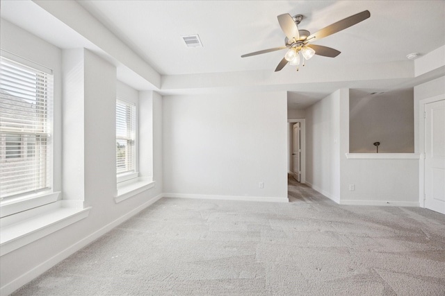 carpeted spare room featuring baseboards, visible vents, and ceiling fan