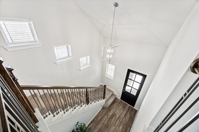 foyer entrance with high vaulted ceiling, an inviting chandelier, dark wood finished floors, and stairs