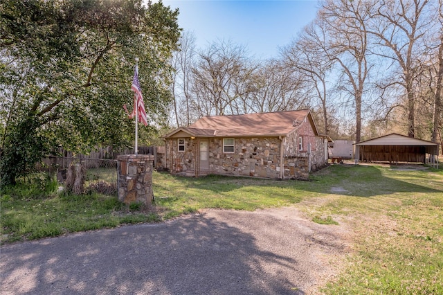 exterior space featuring a detached carport, a front yard, fence, and stone siding