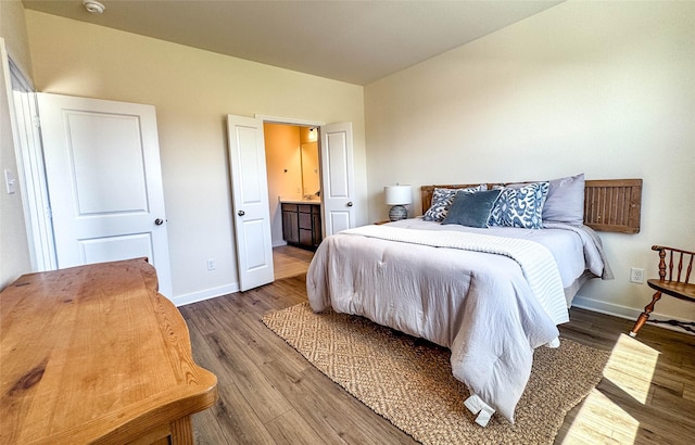 bedroom with ensuite bathroom, baseboards, and wood finished floors