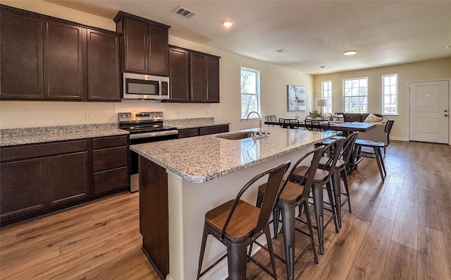 kitchen with visible vents, a kitchen bar, a sink, light wood-style floors, and appliances with stainless steel finishes