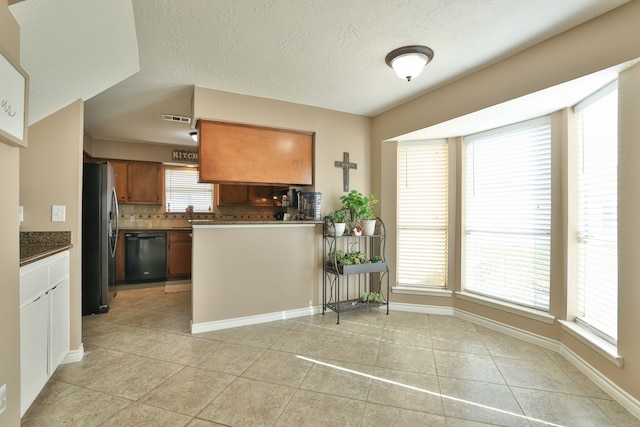 kitchen with light tile patterned flooring, freestanding refrigerator, dishwasher, brown cabinets, and backsplash