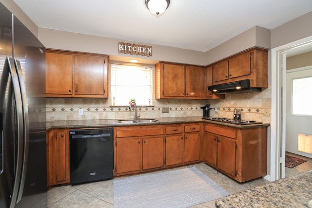 kitchen featuring a wealth of natural light, a sink, under cabinet range hood, black dishwasher, and freestanding refrigerator