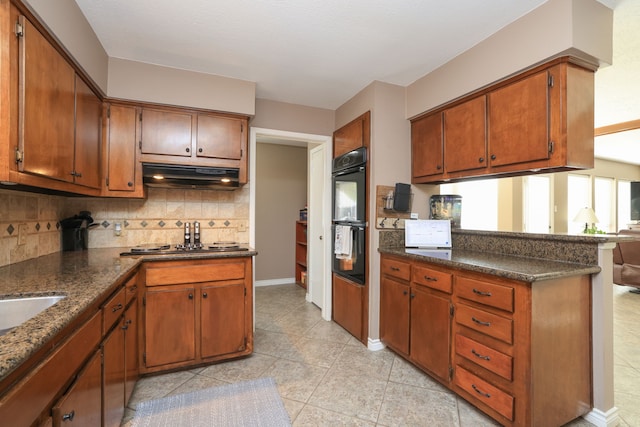 kitchen featuring a peninsula, under cabinet range hood, dobule oven black, brown cabinets, and backsplash