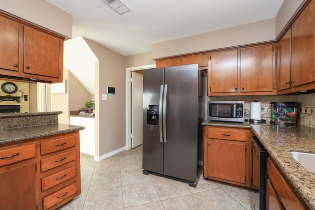 kitchen featuring light tile patterned floors, backsplash, appliances with stainless steel finishes, and brown cabinetry