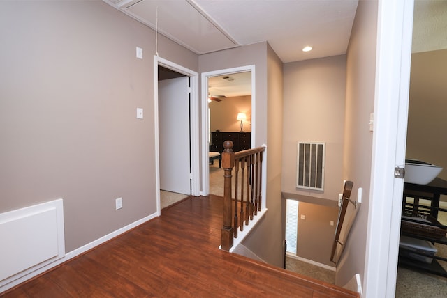 hallway with visible vents, baseboards, attic access, an upstairs landing, and wood finished floors