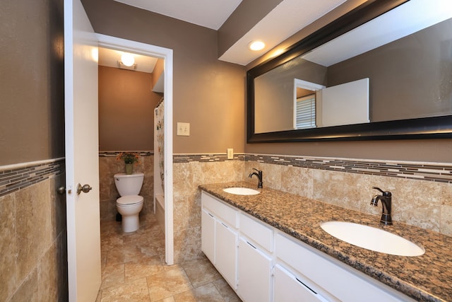 full bathroom featuring double vanity, toilet, a wainscoted wall, and a sink