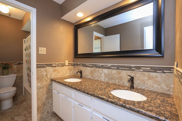 full bathroom with a sink, a wainscoted wall, toilet, and double vanity